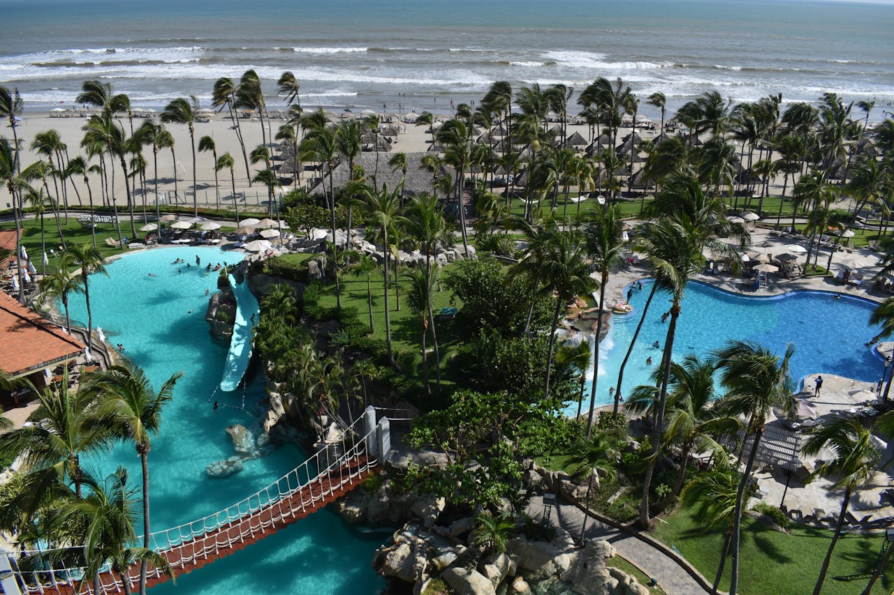 Aerial view of a tropical resort in Acapulco with pools, palm trees and the ocean beyond.
