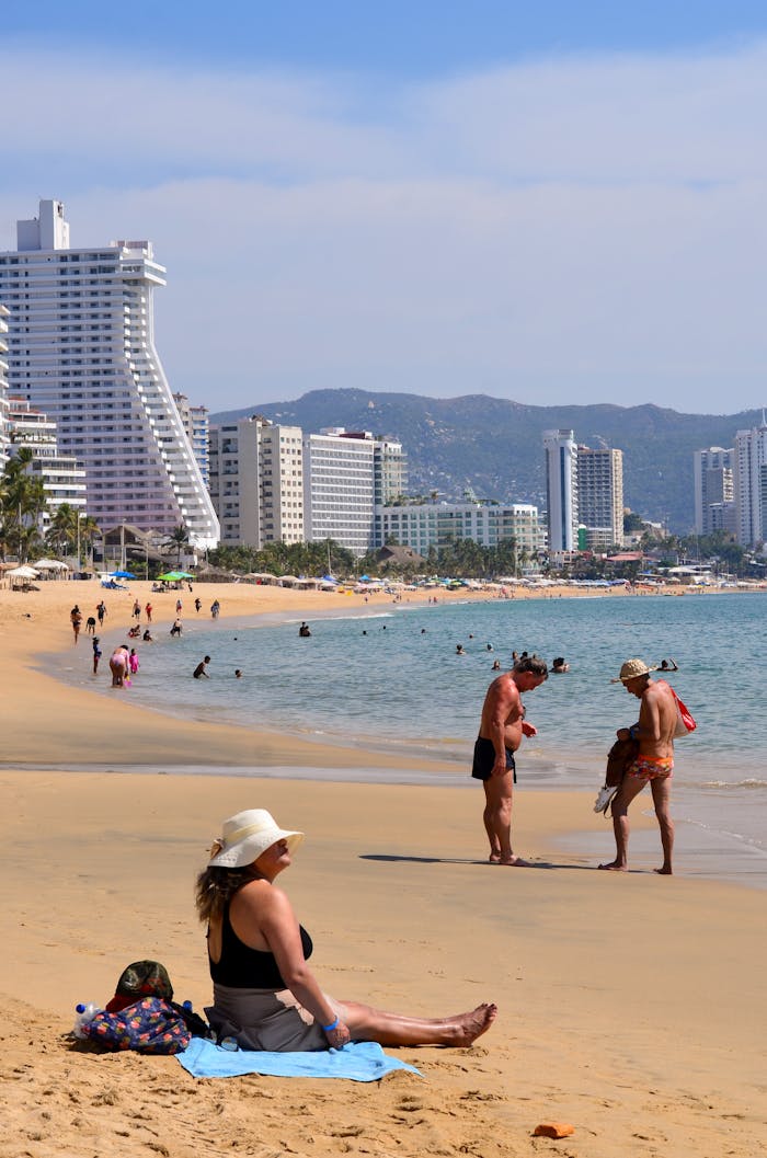 Tourists enjoying a sunny day at the beach in Acapulco, Mexico with high-rise buildings in the background.